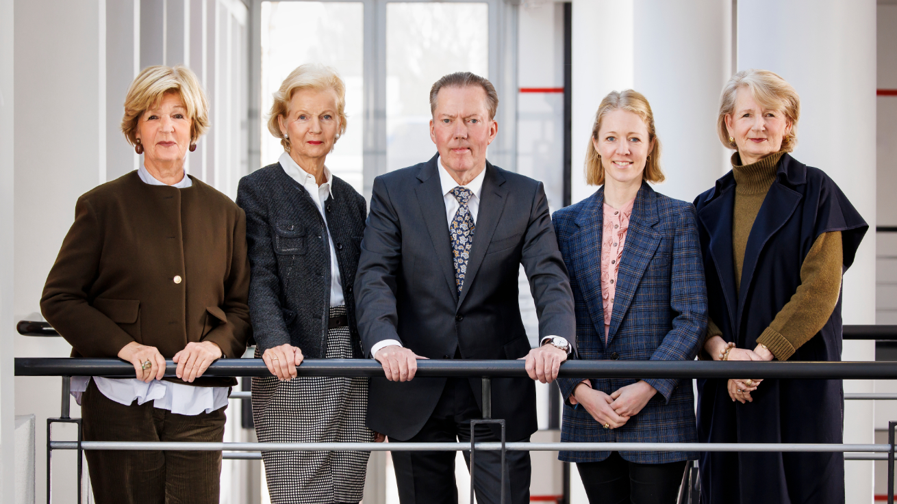 Foundation Board from the Friedel and Walter Hoyer Foundation stand behind a railing in a modern building