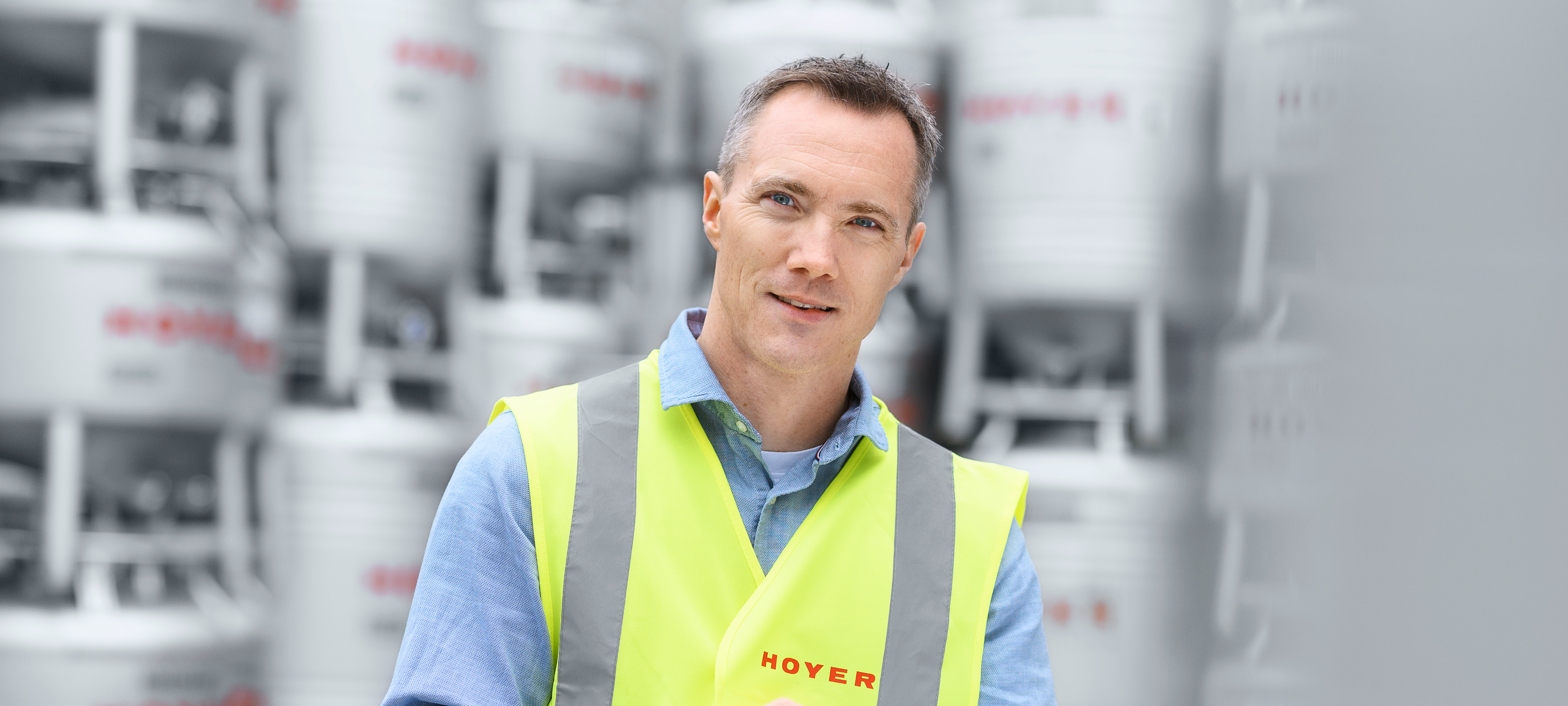 Employee with safety vest and tablet standing in front of stacked HOYER IBCs in the outdoor area