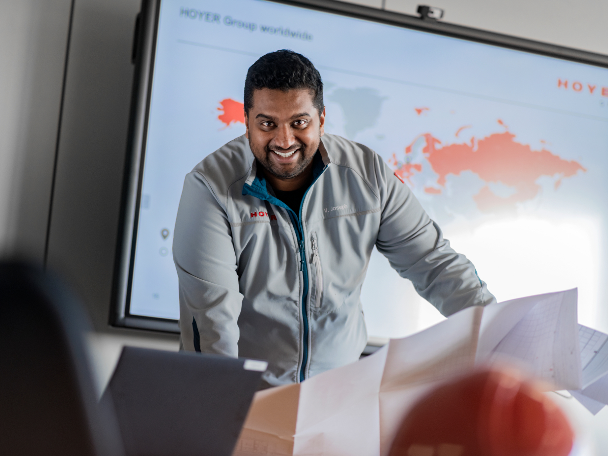 HOYER Group employee in gray jacket standing in front of presentation screen with world map and marked regions