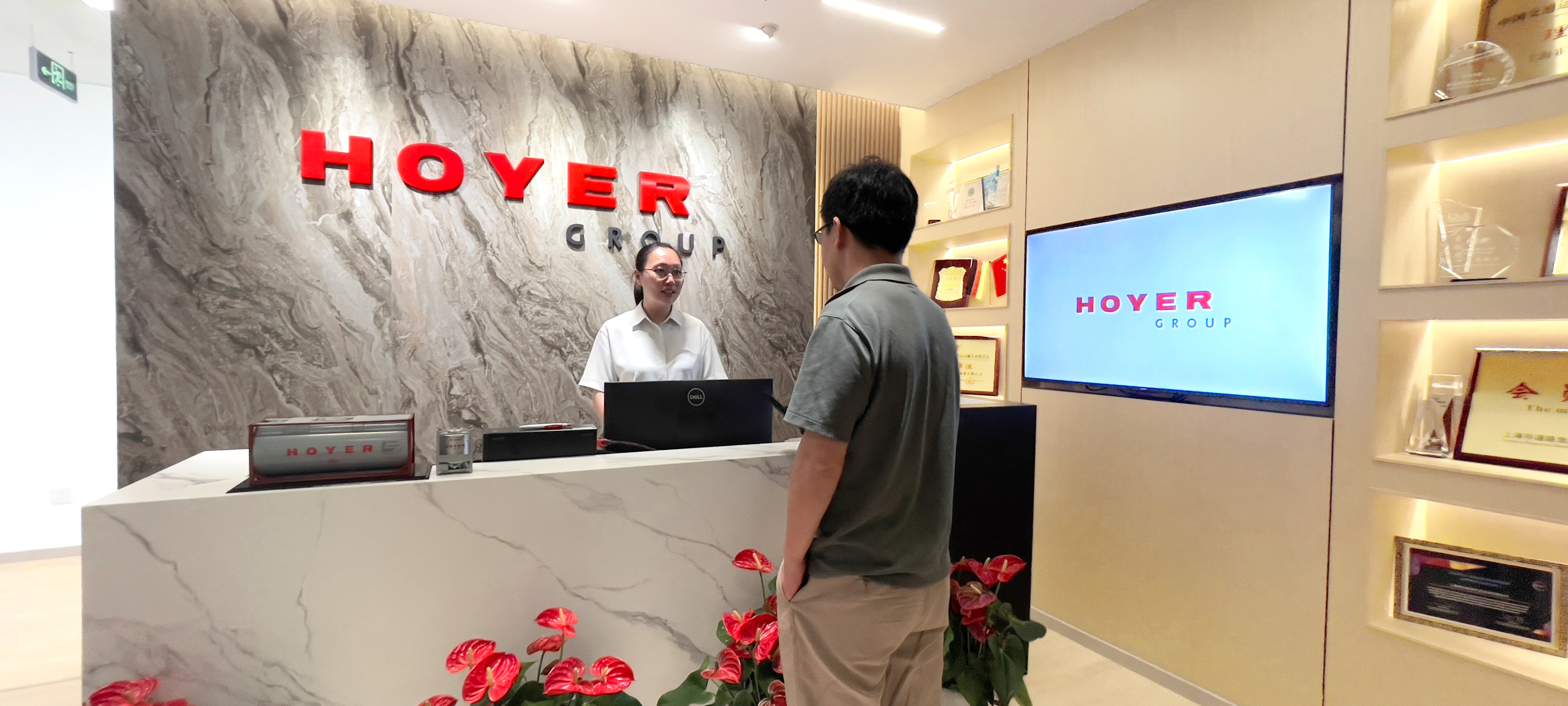 Reception area of HOYER GROUP with branded signage, marble desk, red flowers, and award displays in a modern foyer
