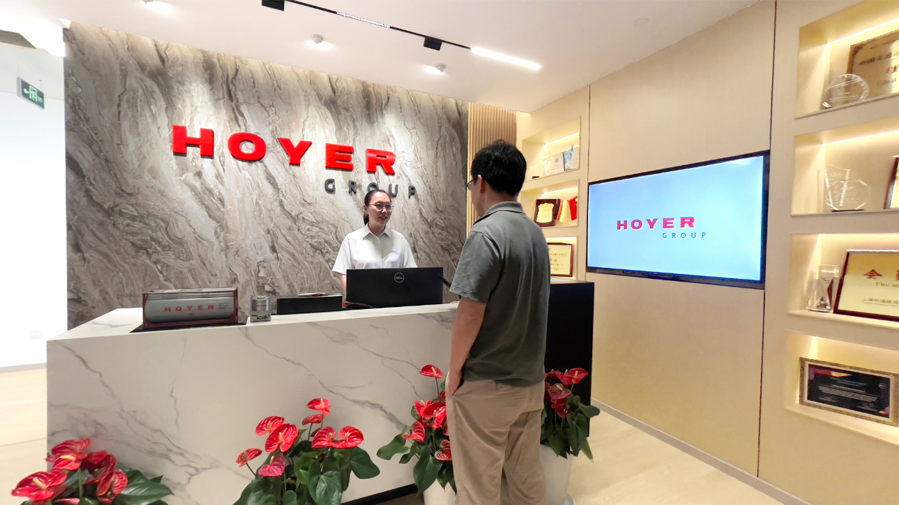 Reception area of HOYER GROUP with branded signage, marble desk, red flowers, and award displays in a modern foyer